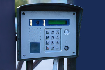 close-up gray iron intercom on a metallic blue fence.