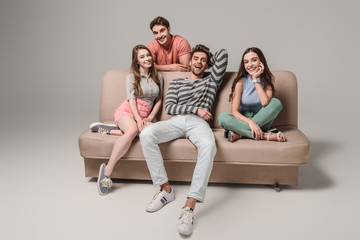 smiling young friends sitting on sofa on grey