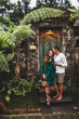 Happy couple in love smiling and kissing on background of traditional balinese architecture. Welcome to travel in Bali concept, vacations honeymoon in Asia.
