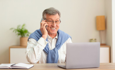 Wall Mural - Senior Businessman Talking On Cellphone Working On Laptop In Office