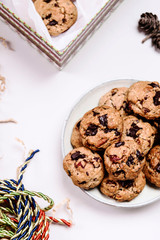 Wall Mural - Christmas cherry, chocolate and pecans oatmeal cookies and gift box  with cookies and corrugated paper filler on grey  background decorated fir cones. Delicious gift. Hygge. Selective focus