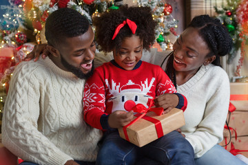 Wall Mural - Cute little black girl opening Christmas gift with her parents