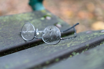 Brille auf Parkbank mit Regentropfen auf Glas