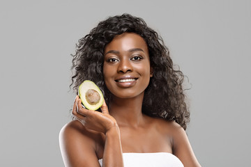 Wall Mural - Portrait of attractive black woman with avocado half over gray background