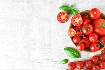 Wall Mural - Fresh tomatoes in bowl on rustic white table top view. Tomato red background healthy food vegetables and ripe basil leaves on old board.