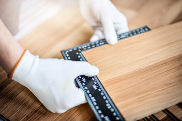 Wall Mural - Close up of wood worker with in white gloves measuring angle and new laminated wooden floor board.