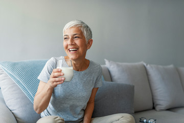 Senior woman's hands holding a glass of milk. Happy senior woman having fun while drinking milk at home. Senior Woman drinking a glass of milk to maintain her wellbeing.....