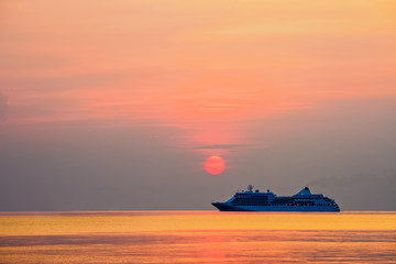 Wall Mural - Travel by Cruise ship in the ocean, large luxury passenger boat is sailing on the bright sea, red sun in the colorful sky is yellow, orange, beautiful nature landscape at sunset or sunrise background