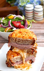 Wall Mural - Sandwich with Parmesan and Gruyere cheese, ham, béchamel sauce and artisan bread accompanied by a salad on a wooden background.  The Croque Monsieur.