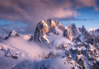 Wall Mural - majestic snowy mountain peaks in fog and blue sky with purple clouds at sunset. winter landscape wit
