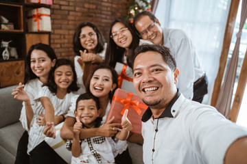 Wall Mural - asian family wearing white take selfie using smartphone together at home on christmas day