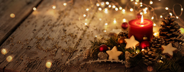 Christmas background - First Advent Sunday - Red Advent candle with natural Xmas decoration, branches and pine cones on rustic wood with magic lights