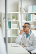 © Seventyfour - Side view portrait of African-American doctor looking at computer screen while sitting at desk in clinic, copy space