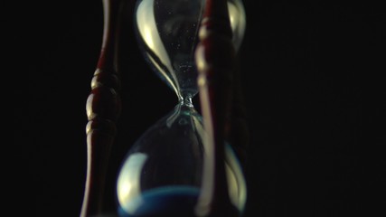 Wall Mural - Hourglass clock time concept. Old vintage wood frame blue sand clock countdown on dark background. Close up.