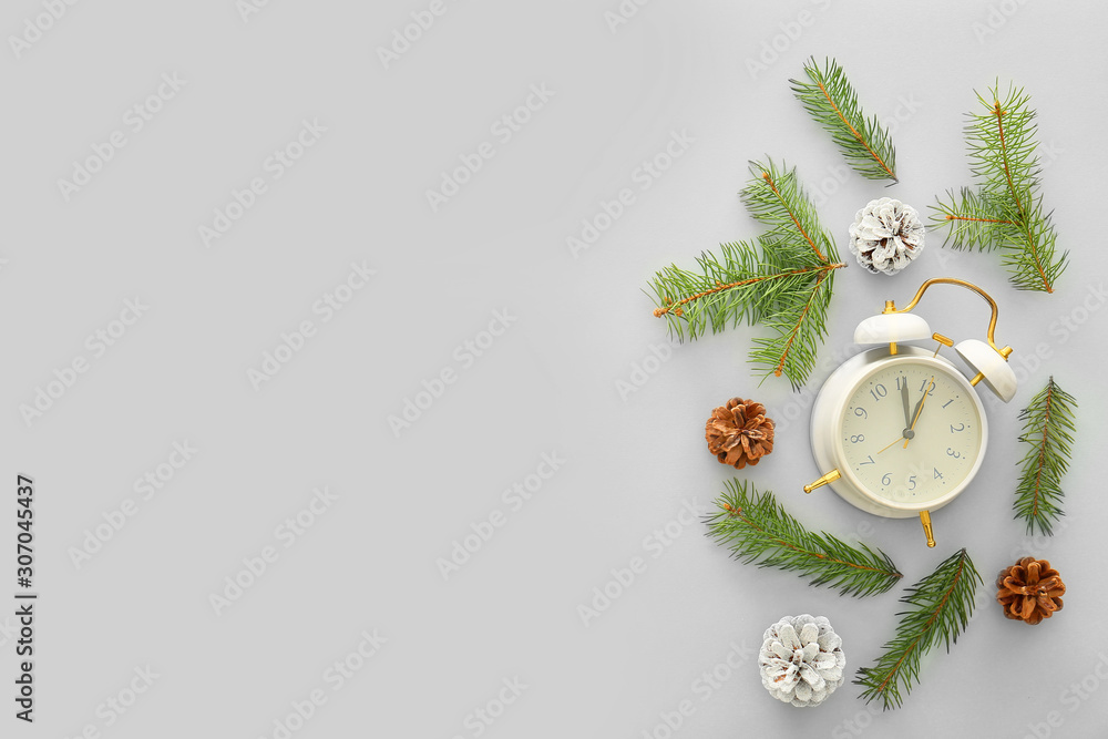 Alarm clock with Christmas fir tree branches and cones on white background