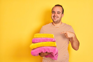 Sticker - Young shopkeeper man holding folded towels standing over isolated yellow background very happy pointing with hand and finger