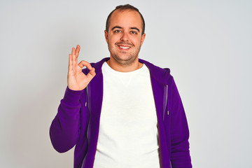 Sticker - Young man wearing purple sweatshirt standing over isolated white background smiling positive doing ok sign with hand and fingers. Successful expression.