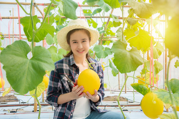 Beautiful asian farmer holding fresh melon that cultivated from her organic farm and smiles.