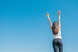 © max_play - Happy woman with tanned slim body breathing fresh air raising her arms up, enjoying a sunny summer holiday on beach destination against blue sky, outdoors. Travel and well being lifestyle.