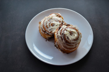 Two classic rolls with cinnamon and cheese cream on top in an open box on a black, dark gray background