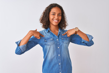 Wall Mural - Young brazilian woman wearing denim shirt standing over isolated white background looking confident with smile on face, pointing oneself with fingers proud and happy.