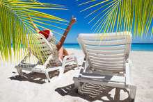 Happy Woman In Santa Helper Hat Lie On Sunbed Showing  Thumbs Up At The Beach