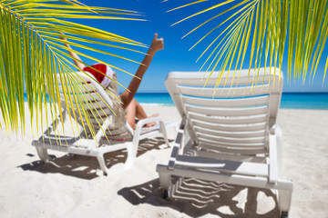 Wall Mural - Happy woman in Santa Helper Hat lie on sunbed showing  thumbs up at the beach