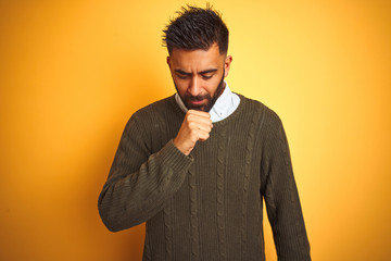 Wall Mural - Young indian man wearing green sweater and shirt standing over isolated yellow background feeling unwell and coughing as symptom for cold or bronchitis. Healthcare concept.