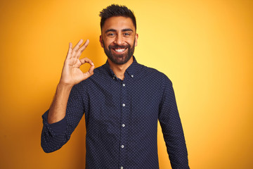 Sticker - Young handsome indian businessman wearing shirt over isolated yellow background smiling positive doing ok sign with hand and fingers. Successful expression.