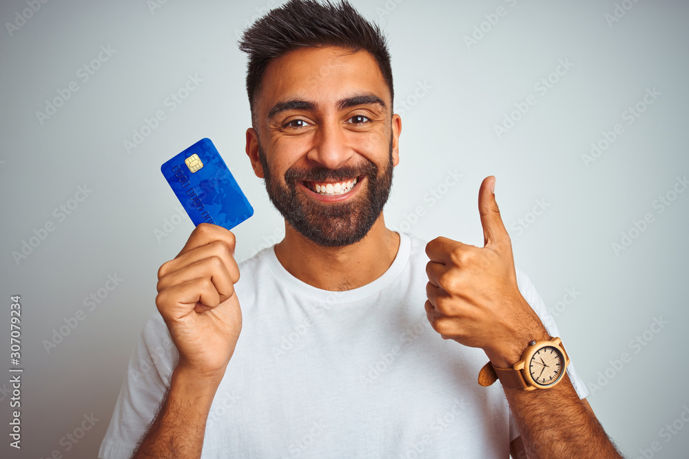 Young indian customer man holding credit card standing over isolated ...
