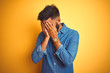 © Krakenimages.com - Young indian man wearing denim shirt standing over isolated yellow background with sad expression covering face with hands while crying. Depression concept.