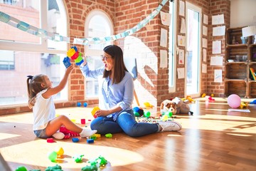 Caucasian girl kid playing and learning at playschool with female teacher. Mother and daughter at playroom around toys playing with bulding blocks