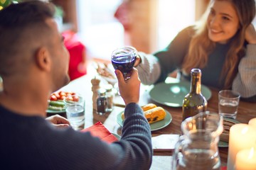 Wall Mural - Young beautiful couple smiling happy and confident. Eating food and toasting with cup of wine celebrating christmas at home