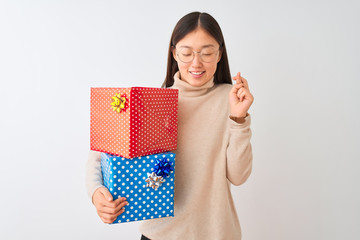 Sticker - Young chinese woman holding birthday gifts over isolated white background gesturing finger crossed smiling with hope and eyes closed. Luck and superstitious concept.