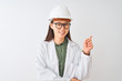 © Krakenimages.com - Young chinese engineer woman wearing coat helmet glasses over isolated white background with a big smile on face, pointing with hand and finger to the side looking at the camera.
