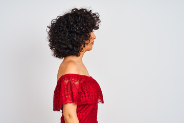 Young arab woman with curly hair wearing red dress standing over isolated white background looking to side, relax profile pose with natural face with confident smile.