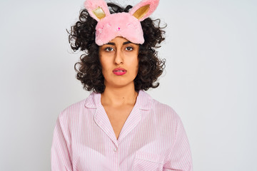 Sticker - Arab woman with curly hair wearing pajama and sleep mask over isolated white background Relaxed with serious expression on face. Simple and natural looking at the camera.