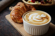 A cup of coffee with latte art on top, butter  croissant and granola with fresh tropical fruits and yogurt on table in caffee. Concept of healthy breakfast