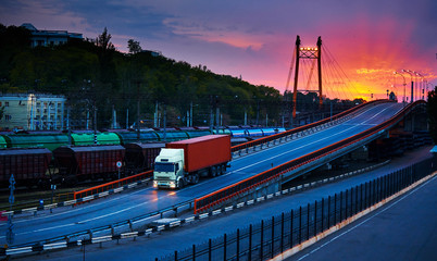 truck with container rides over the bridge, beautiful sunset, freight cars in industrial seaport, the road goes up