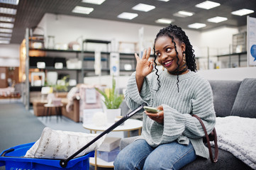 Wall Mural - African woman with mobile phone and shopping basket in a modern home furnishings store.