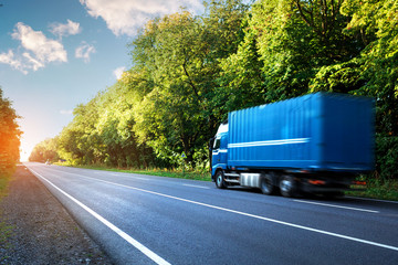 Wall Mural - Arriving blue truck on the road in a rural landscape at sunset