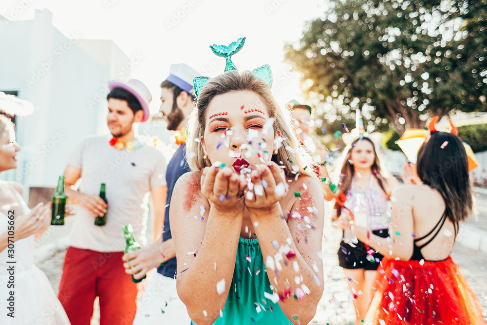 Brazilian Carnival. Young woman in costume enjoying the carnival party blowing confetti - obrazy, fototapety, plakaty 
