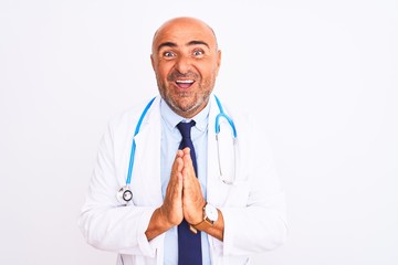 Middle age doctor man wearing stethoscope and tie standing over isolated white background praying with hands together asking for forgiveness smiling confident.