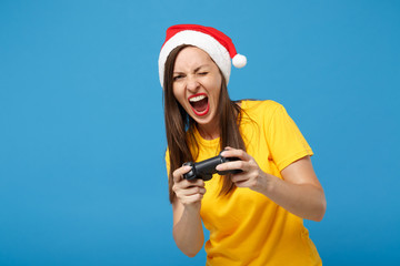 Poster - Crazy young woman Santa girl in Christmas hat posing isolated on blue wall background. Happy New Year 2020 celebration holiday concept. Mock up copy space. Hold joystick play game screaming, blinking.