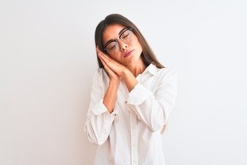 Wall Mural - Young beautiful businesswoman wearing glasses standing over isolated white background sleeping tired dreaming and posing with hands together while smiling with closed eyes.