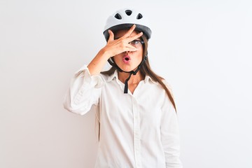 Poster - Beautiful businesswoman wearing glasses and bike helmet over isolated white background peeking in shock covering face and eyes with hand, looking through fingers with embarrassed expression.