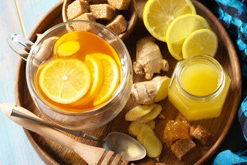 Wall Mural - Cup of hot tea with lemon, ginger, honeycomb and honey close-up on a wooden table.