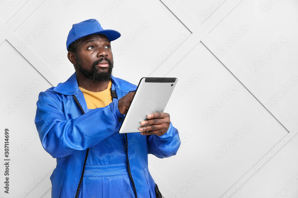 African-American car mechanic with tablet computer near light wall