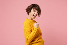 Side View Of Young Brunette Woman Girl In Yellow Sweater Posing Isolated On Pastel Pink Background Studio Portrait. People Sincere Emotions Lifestyle Concept. Mock Up Copy Space. Doing Winner Gesture.