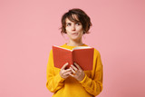 Fototapeta  - Pensive young brunette woman girl in yellow sweater posing isolated on pink wall background, studio portrait. People sincere emotions lifestyle concept. Mock up copy space. Holding and reading book.